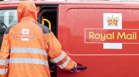 Getty Images A Royal Mail worker in a fluorescent hooded jacket stands with their back turned to the camera beside a Royal Mail van.