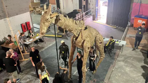 Photograph of a puppet giraffe underneath a railway arch in Manchester city centre.