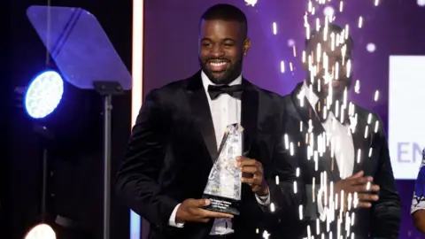 UK Athletics sprinting coach Leon Baptiste collects an award for coach of the year at a 2023 awards ceremony