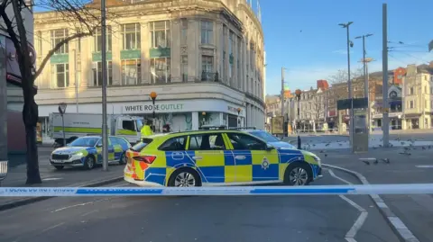 BBC Police tape with a number of police vehicles parked behind