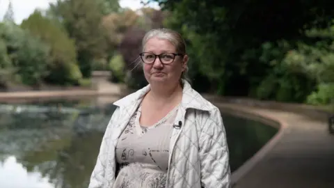 Ben Moore/BBC Jo Lazzam is standing in front of a lake in a park in Tunbridge Wells, Kent