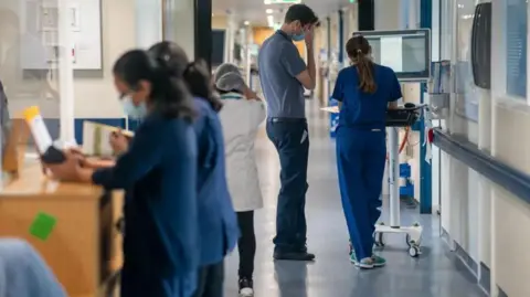 PA Media Doctors and nurses walking and standing in a busy hospital corridor.