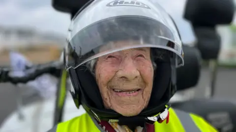 Genna Brown is smiling and wearing a motorbike helmet and yellow high vis jacket.