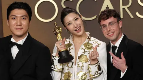 Jeong Hoon Seo, Ejae and songwriter Mark Sonnenblick posing with their Oscar 2026 Best Original Song award for Golden the theme song of Kpop Demon Hunters