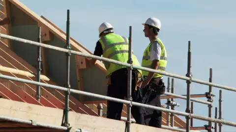 Getty Images Two builders standing on a scaffolding working on a roof