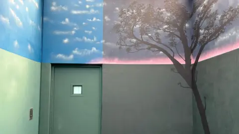 Image of the mural soft dark grey and green colour tones at the base and a  night and day transition at the top. There is a tree in the night scene.