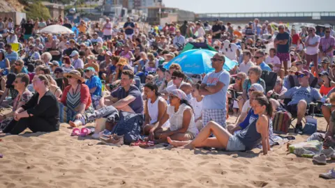 Stephen Gatehouse Crowds of people sat on the beach staring towards the water