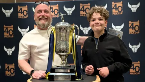 Neil McManus Neil McManus and a young child standing next to Oxford United's Milk Cup.