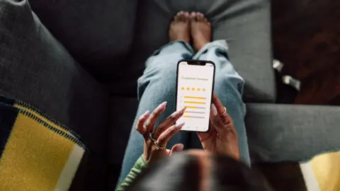 Getty Images Stock photo shows an overhead view of a person holding a smartphone with a screen saying 'customer feedback' and a star rating interface, as they sit on the sofa at home.