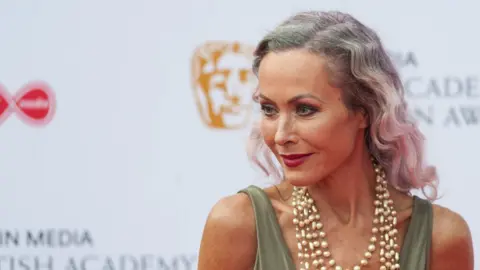 Amanda Mealing on the red carpet at the Bafta television awards. She has dark grey hair and is wearing a blue dress top and pearl necklace.