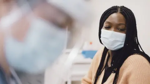 Getty Images A doctor wearing a mask, blurred in the foreground with a patients, also wearing a mask, in the background