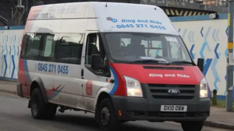LDRS A white minibus with red and blue patterns being driven on the road. 