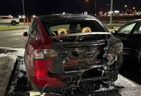 US Justice Department The back end of a burnt-out red car pictured at night in a parking lot