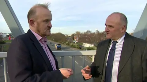 Two men in suits arguing on a bridge over a major road