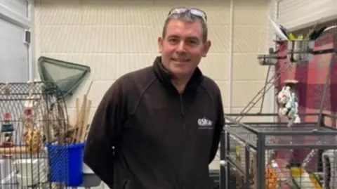 BBC a picture of GSPCA manager Steve Byrne pictured at the charity. He is wearing a black quarter zip and is stood around animal enclosures.
