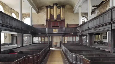 Historic England General view of interior showing nave box pews in oak arranged in 2 double rows and organ with its original mahogany case.