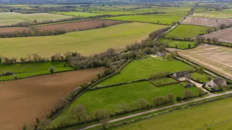PA An aerial view of the Wiltshire countryside with green fields, farm buildings and an old Roman road going diagonally through the landscape into the distance