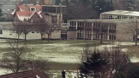 Getty Images A large 1970s concrete school in a brutalist style in a playing field. Some snow is on the ground and the trees are bare. A sole man can be seen from the back near the field, at a distance.