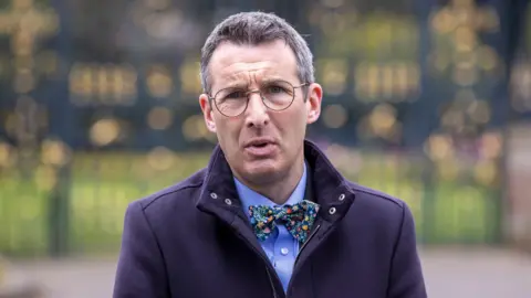 Liam McBurney/PA Wire Muir is outside. He's talking. He wears glasses. He has a navy coat on with a blue shirt and floral bow tie. 