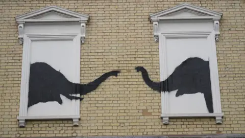 PA Media Banksy artwork depicting two elephants reaching out to one another from building's false windows