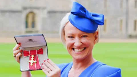 PA Media Ruth wearing a blue hat and dress holding her OBE