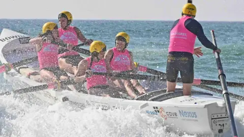 Lifesaving World Championship Members of Perranporth Surf Lifesaving Club rowing a boat on choppy water. They are wearing pink lifejackets and yellow helmets