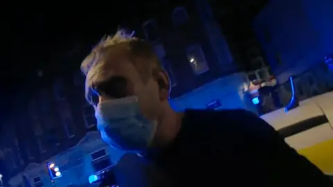 A man wearing a face mask being arrested.