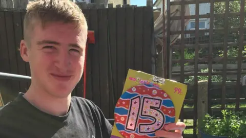 Handout A boy with blonde hair and a black top. He holds a birthday badge.