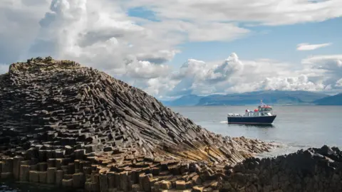 A tour boat passes Staffa and one of its basalt rock formations.