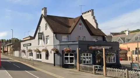 Google A Google street view image of the Whyteleafe Tavern, which is grey and has hanging baskets of flowers over the windows. 