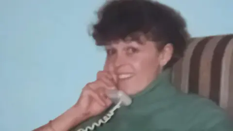 Wendy Hughes An old colour photo of a woman sitting on an armchair speaking on the phone. 