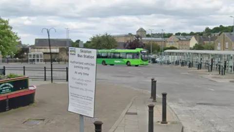 General view of Skipton Bus Station, with bollards and a green single-decker bus in the background.