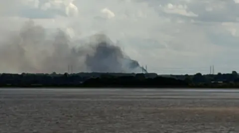 Richard Madden/BBC Plumes of smoke rise into the sky. There is a field in the foreground.