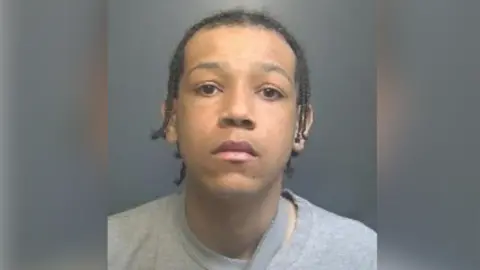 A police custody image showing Nehemiah McIvor-Murray with black hair wearing a grey, round-necked T-shirt. 