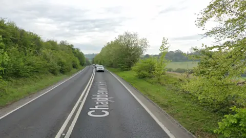 A two-lane road with cars driving on it with trees and bushes along both sides.