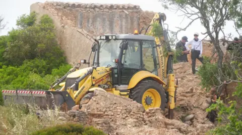 Search teams use a backhoe digger next to a derelict and abandoned property close to Praia De Luz, Portugal, where searches are being carried out by officers investigating the disappearance of Madeleine McCann, in countryside a few miles from the resort where she was last seen in 2007.