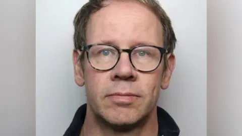 Staffordshire Police A police mugshot of Matthew Isles. He is wearing glasses and is standing against a pale background.