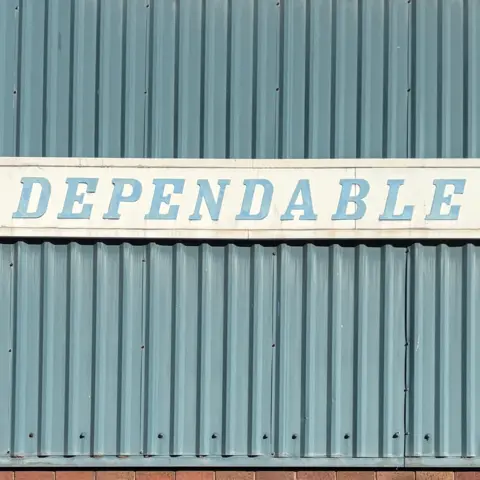 Tom Hicks A blue corrugated exterior of a factory wall with a white banner and the blue lettering: DEPENDABLE 