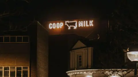 An illuminated sign which reads COOP MILK with an outline of a cow