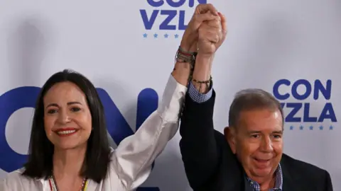 JUAN BARRETO/AFP via Getty Images Venezuelan opposition leader Maria Corina Machado hold hands up with opposition presidential candidate Edmundo Gonzalez Urrutia in Caracas on July 29, 2024, a day after the Venezuelan presidential election. P