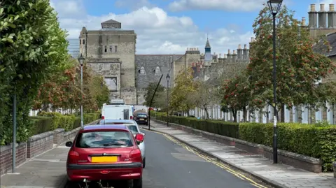 A tree lined street in the railway village with rows of houses and cars parked