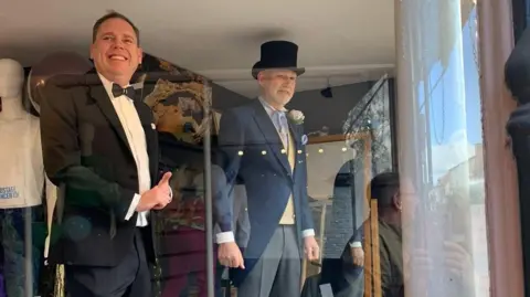 Alec W G Hall Ltd Charlie wears a black suit and dicky bow tie and Mark wears a blue striped suit with a top hat.