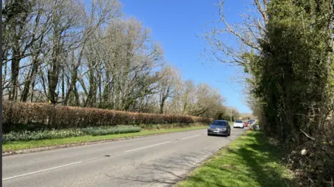 BBC A499 showing cars approaching, trees and grass verge