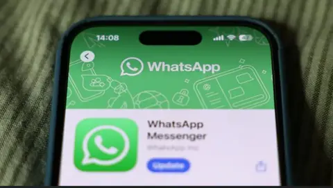 Getty Images The close-up of the top half of a smartphone screen. It is displaying the WhatsApp application. The phone is lying on a green piece of material with darker green horizontal stripes.