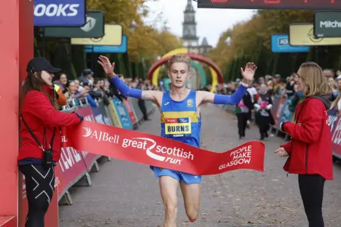 Świetny szkocki bieg Jamie Burns w niebieskim biegu łamie wstążkę, gdy wygrywa półmaraton męski