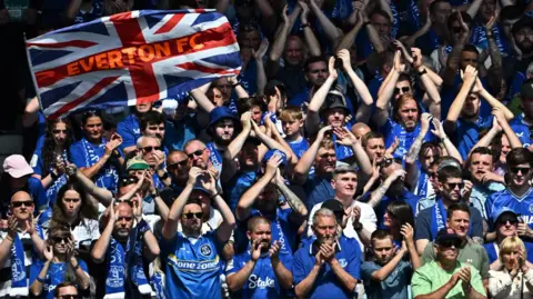 Supporters in blue applaud during the club's emotion last match at Goodison alongside a flag