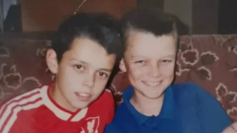 Graeme, a young boy with a Liverpool t-shirt and his brother, in a blue t-shirt, they both smile brightly.