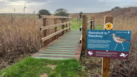 Suffolk County Council Part of the coast path featuring a wooden bridge and sign saying 'Ramsholt to Bawdsey'
