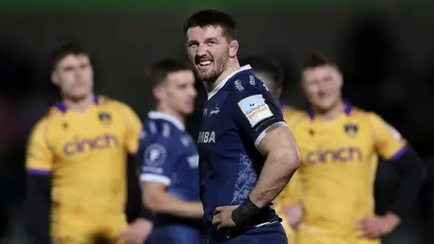 Tom Curry grimaces as he turns around, hands on hips, during Sale's game against Northampton in January