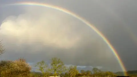 Getty Images A rainbow arcing across an overcast sky with the trace of a second one above, and a line of autumnal trees across the bottom of the scene